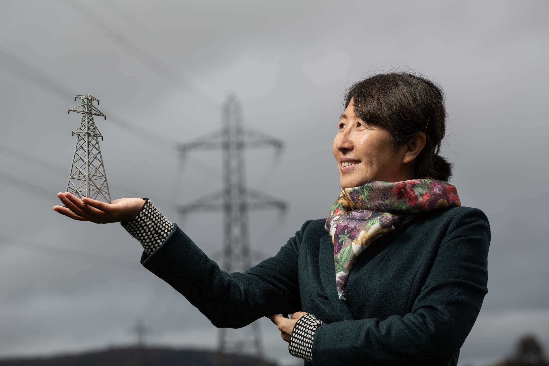 Professor Furong Li holds a model pylon in front of a full-size pylon. Credit: Tim Gandder / University of Bath