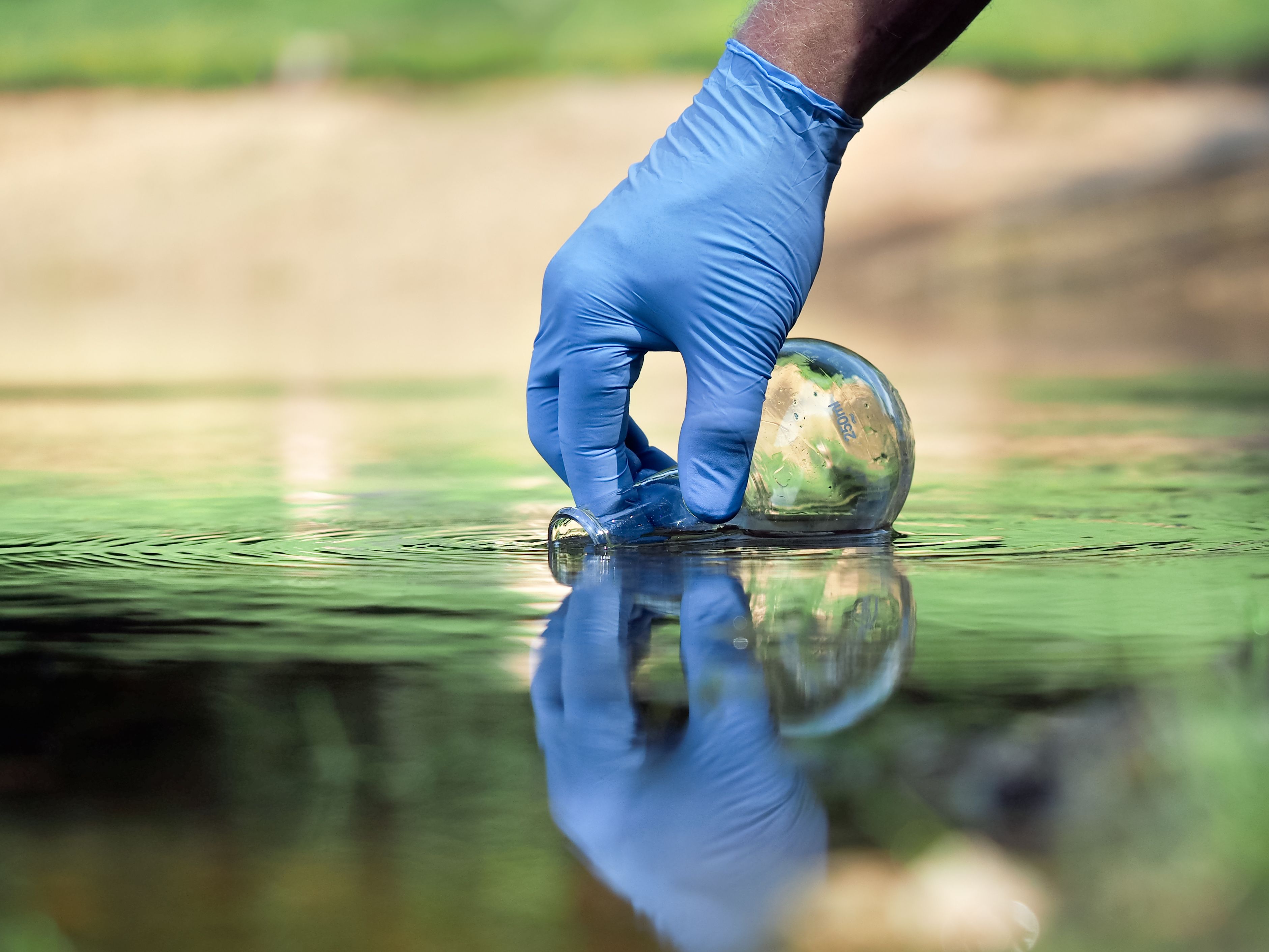 Gloved hand collecting water sample in a river